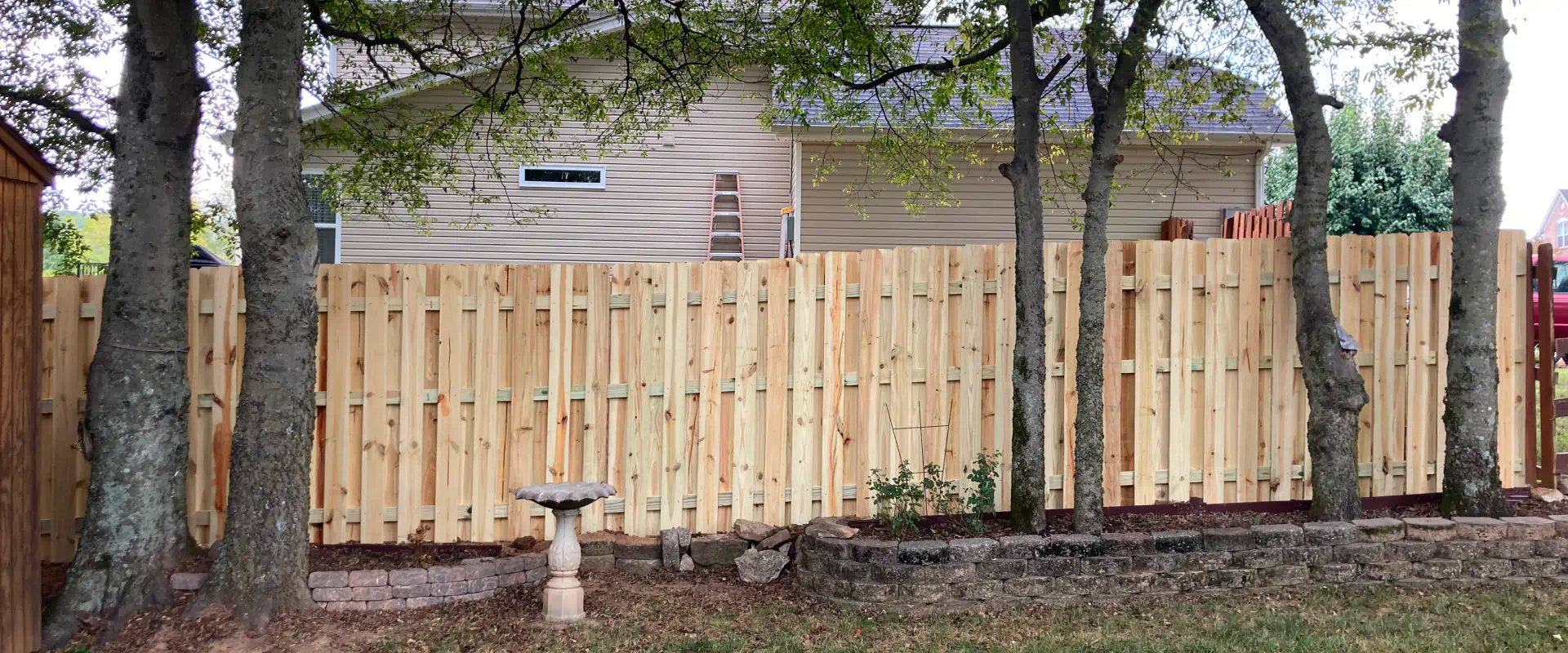 wood fence outside of a beige house with grey roofing and some grass around